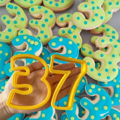 Moule number cake de couleur jaune avec le chiffre 3 et 7 dans la main