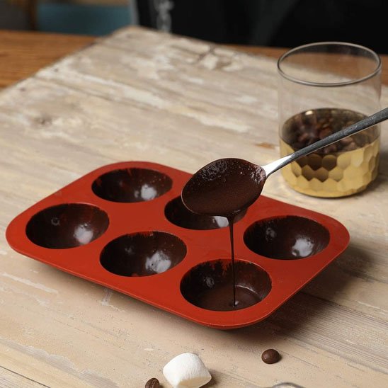 Moule à gâteau en silicone a moitié rempli avec du chocolat avec une cuillère