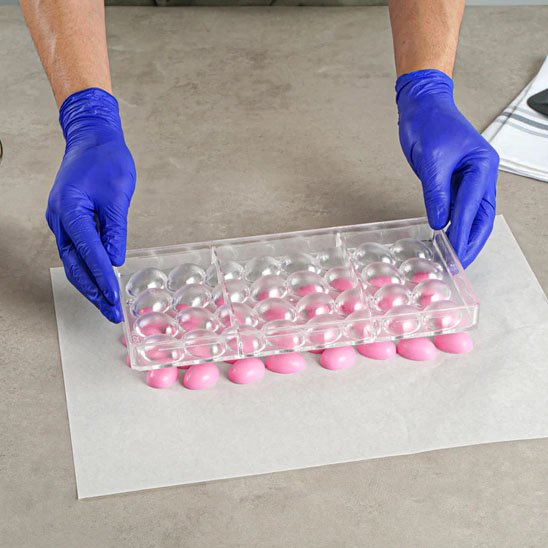 Moule à chocolat transparent avec chocolat rose sur papier blanc