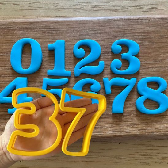 Moule number cake de couleur jaune avec le chiffre 3 et 57 dans la main et de 0 à 8 de couleur bleu
